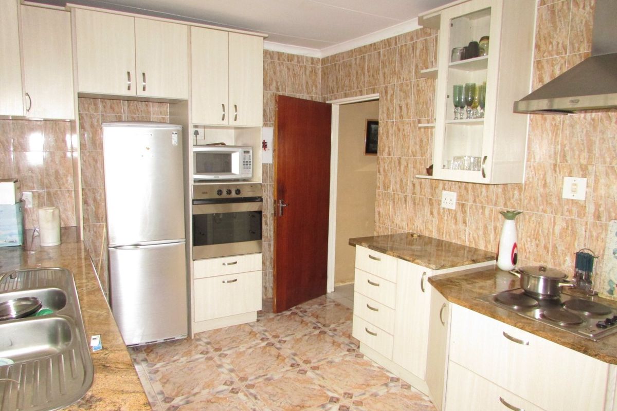 A functional kitchen featuring built-in cabinetry, laminate countertops, a stainless steel sink, and integrated appliances with dated tiled finishes throughout.