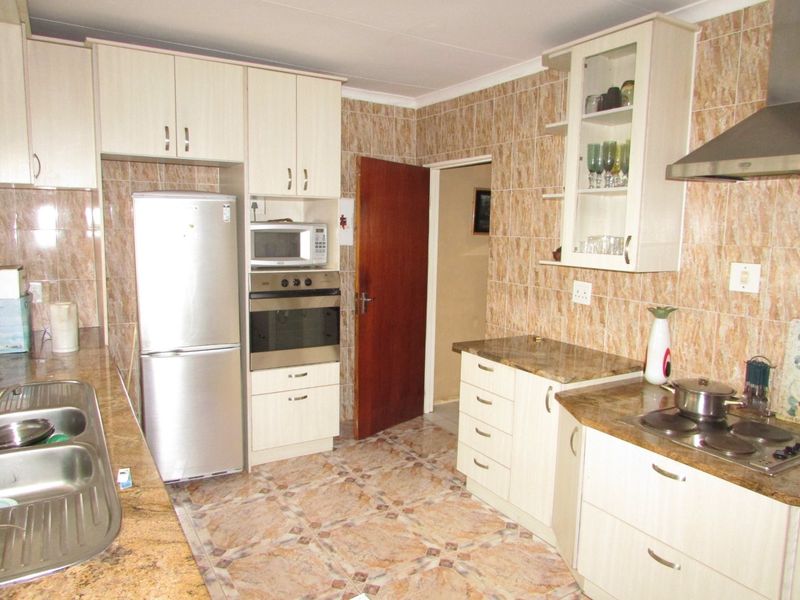 A functional kitchen featuring built-in cabinetry, laminate countertops, a stainless steel sink, and integrated appliances with dated tiled finishes throughout.