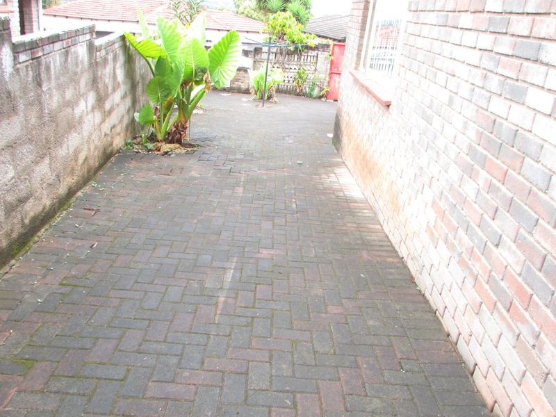 A side or rear exterior walkway featuring brick paving and brick boundary walls, showing signs of weathering and moss accumulation.