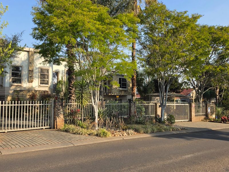 Front exterior view of the property featuring stone cladding, secure metal fencing, and a paved driveway entrance from the street.