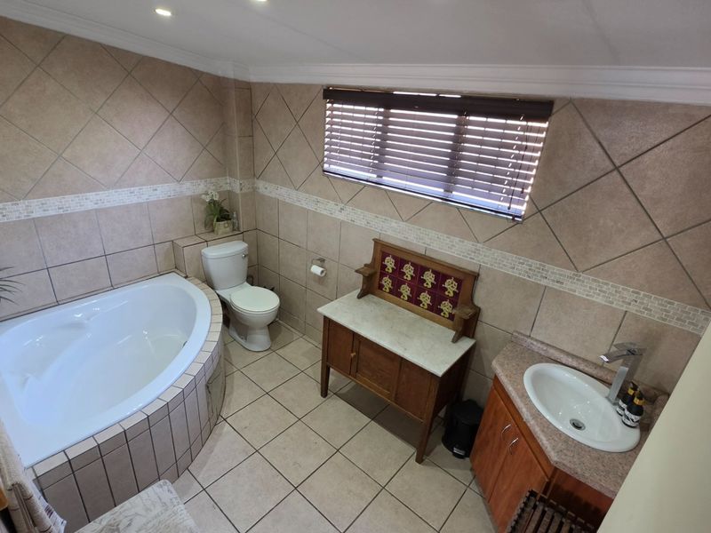 A well-maintained bathroom featuring a corner bathtub, a vanity with a basin, and neutral wall and floor tiling.