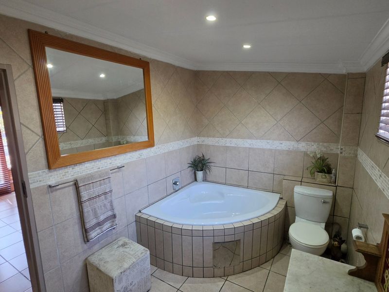A functional bathroom featuring a corner bathtub, tiled wall finishes, and neutral floor tiles, providing a practical layout with natural light from the window.