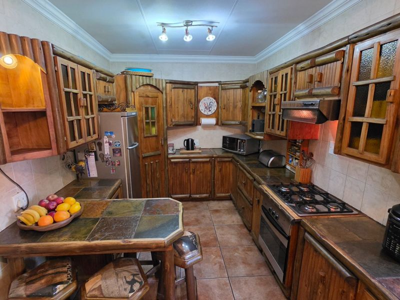 A rustic-style kitchen featuring custom wooden cabinetry, stone tile countertops, a gas hob, built-in oven, and tiled flooring throughout.
