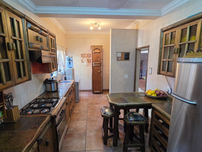 A functional kitchen featuring rustic wooden cabinetry, a gas hob, built-in oven, and tiled finishes throughout.