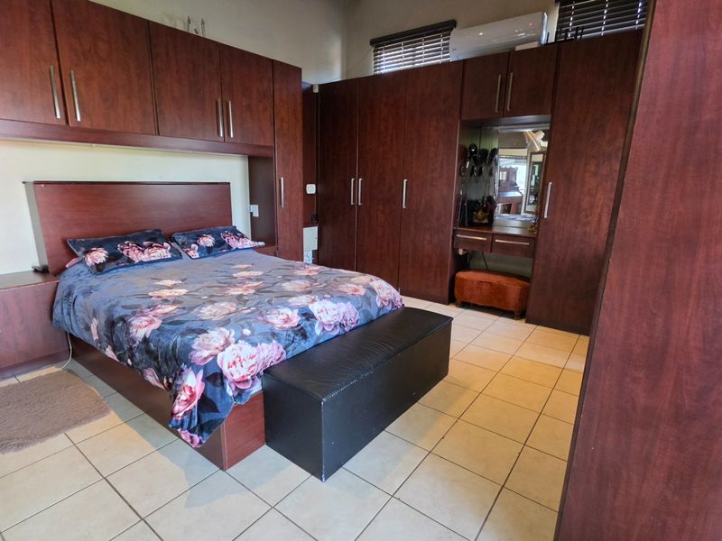 Spacious bedroom featuring extensive dark wood built-in cabinetry, tiled flooring, and a wall-mounted air conditioning unit.