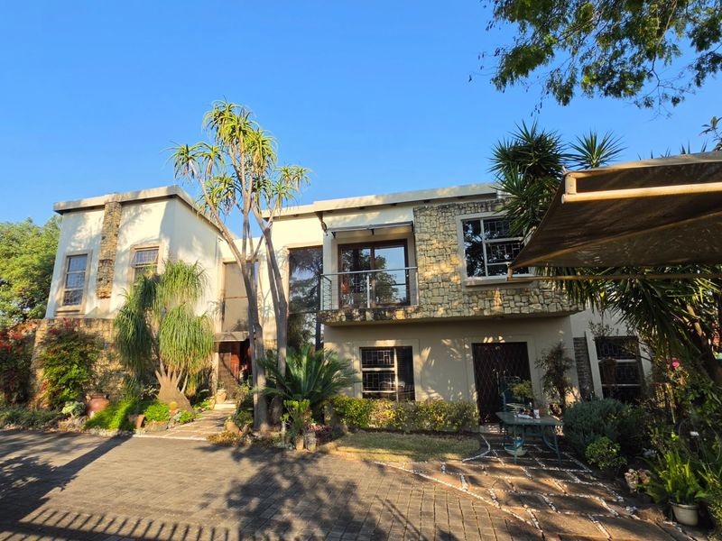 Front elevation of a two-story house featuring stone cladding, a balcony, and a paved driveway with established garden landscaping.