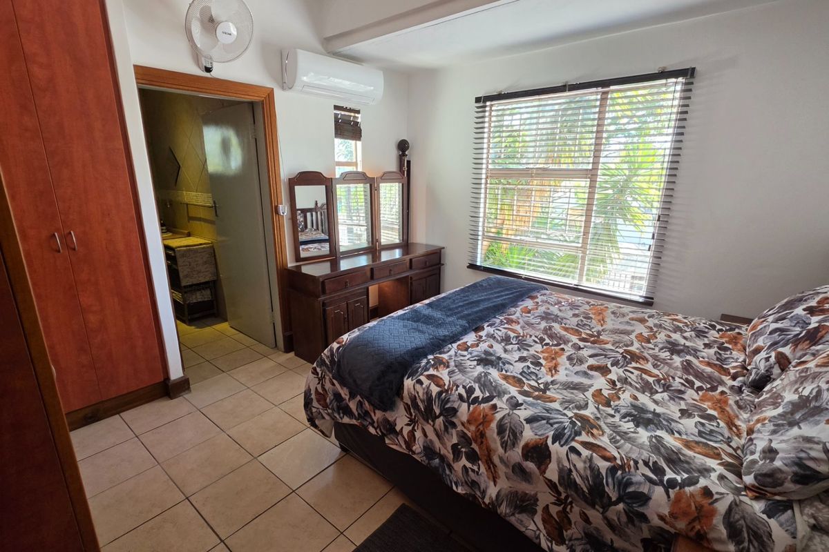A well-maintained bedroom featuring tiled flooring, built-in cupboards, a split-system air conditioner, and a window with venetian blinds, with an adjoining bathroom.