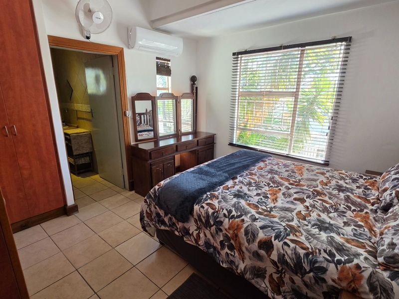 A well-maintained bedroom featuring tiled flooring, built-in cupboards, a split-system air conditioner, and a window with venetian blinds, with an adjoining bathroom.