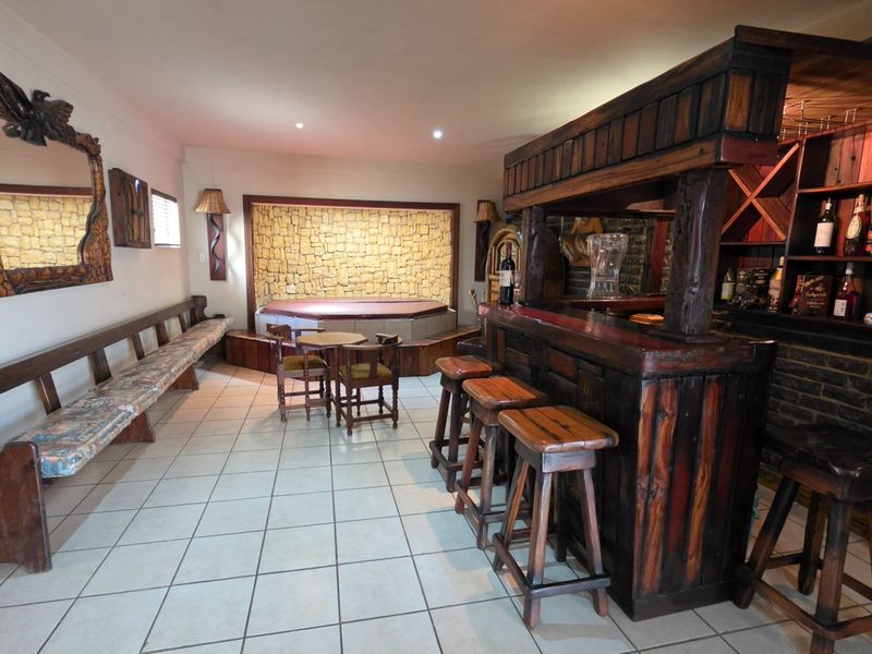 A dedicated entertainment bar area featuring a built-in wooden bar, wine storage, and a sunken spa bath set against a stone feature wall.