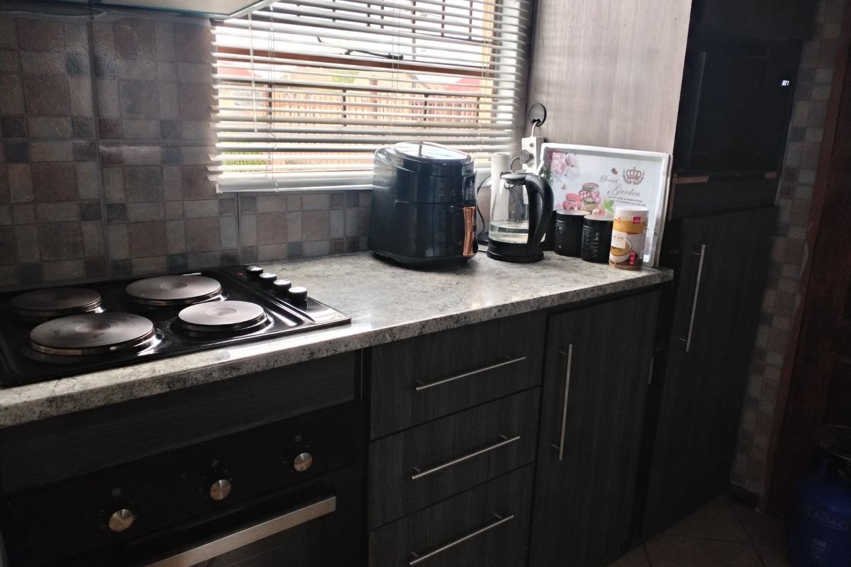 A functional kitchen area featuring dark wood-look cabinetry, a built-in oven with an electric hob, and stone-effect laminate countertops.