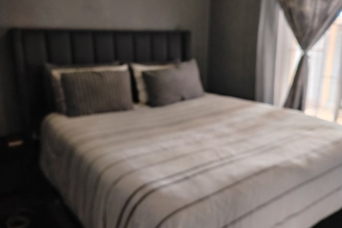 A bedroom featuring a dark upholstered headboard and window treatments.
