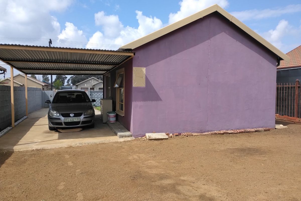 Rear view of the property featuring a metal carport, concrete driveway, and an unfinished exterior wall section with an unlandscaped yard.