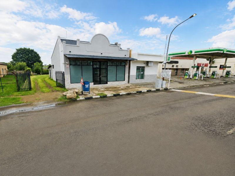 Front view of a commercial property featuring a storefront facade, adjacent to a fuel station with paved access.