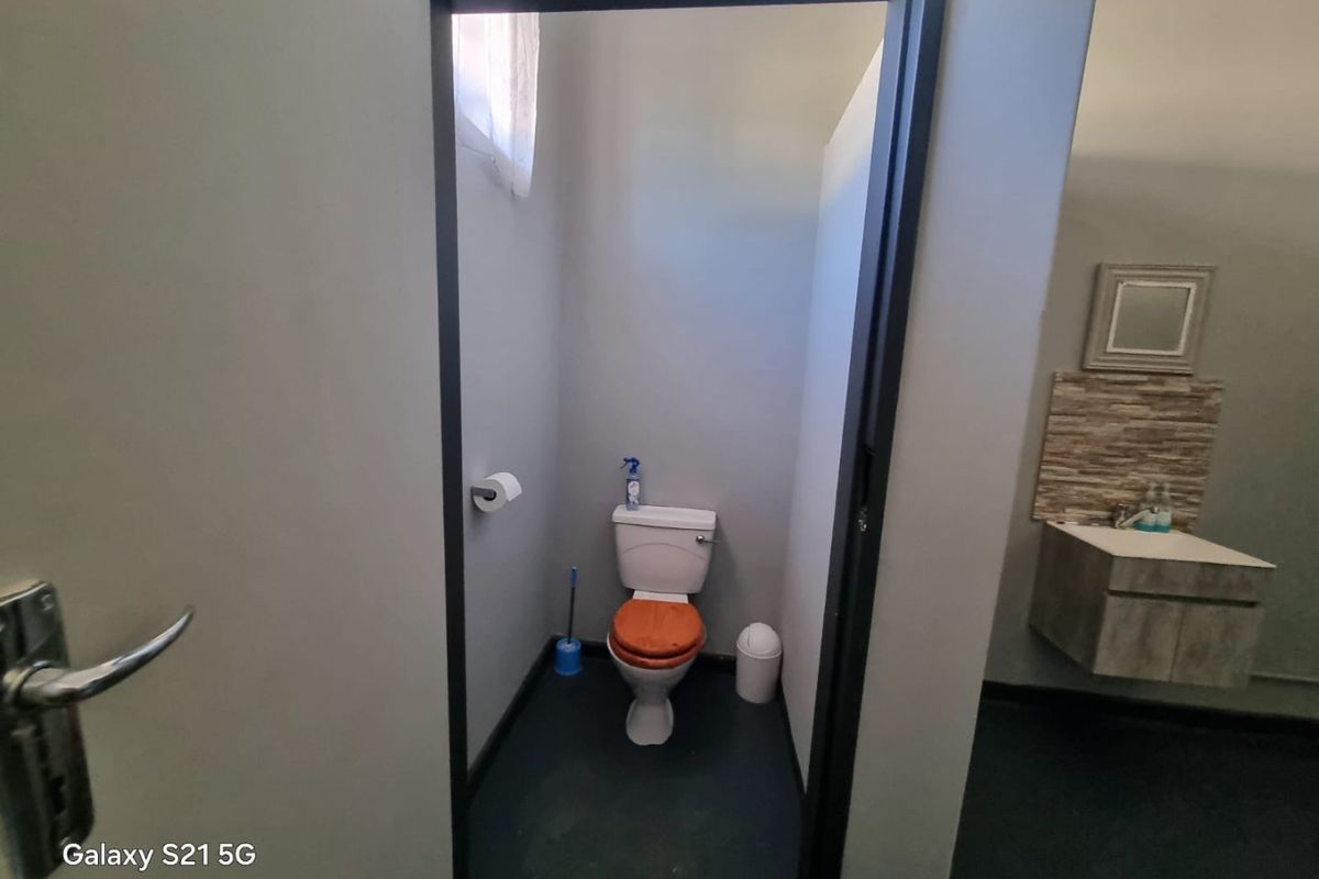 A compact bathroom featuring a toilet and a wall-mounted vanity with a tiled splashback and mirror.