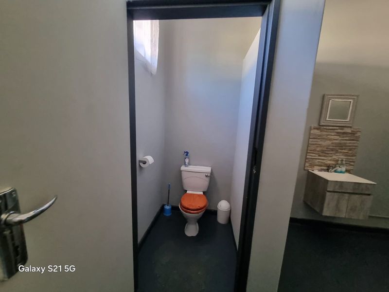 A compact bathroom featuring a toilet and a wall-mounted vanity with a tiled splashback and mirror.