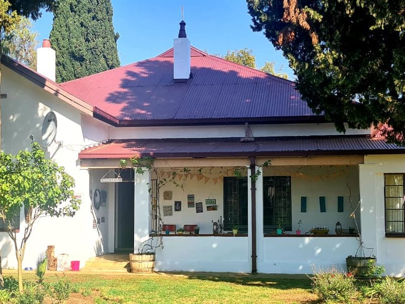 A charming single-story house featuring a red corrugated metal roof, a spacious covered veranda, and established garden surroundings.