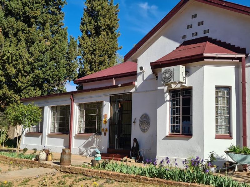 A single-story residential property featuring a metal roof, security bars on windows, and an exterior air conditioning unit, set within a garden area.