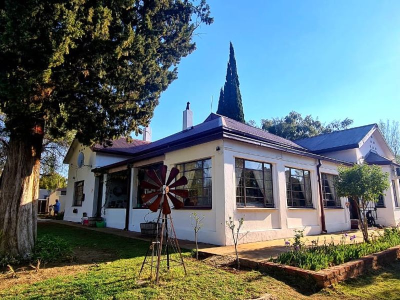 A view of the rear elevation of the house, featuring a well-maintained garden, mature trees, and classic casement windows.
