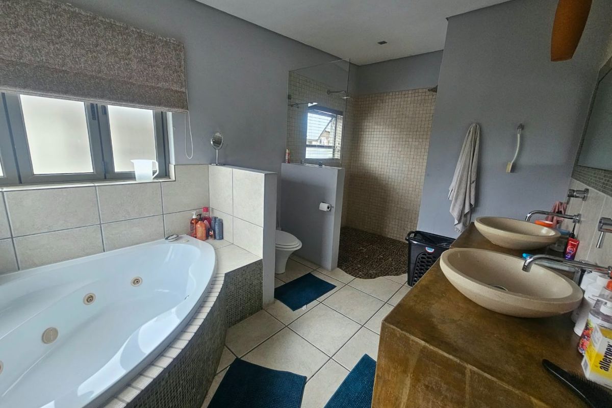 Spacious bathroom featuring a corner spa bath, walk-in shower with pebble flooring, and a double vanity with stone basins.