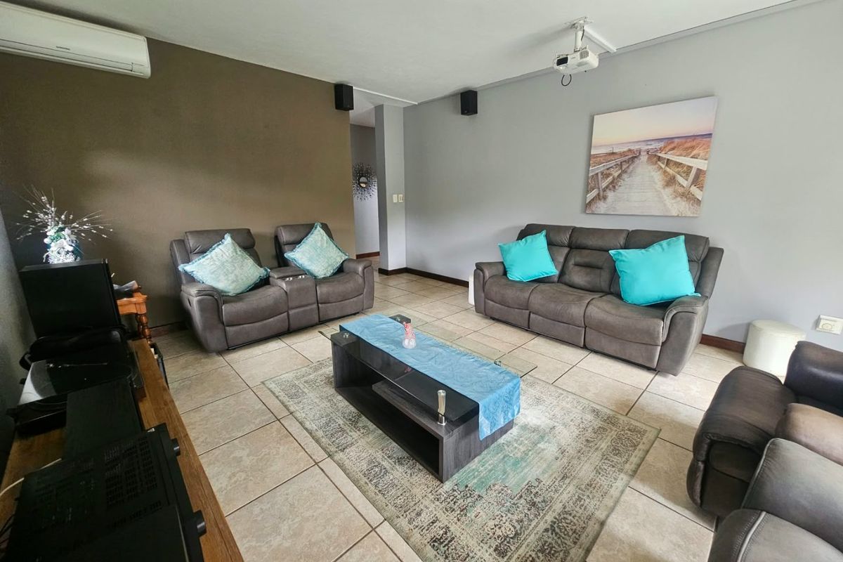 A spacious living room featuring ceramic floor tiles, a ceiling-mounted projector, and a wall-mounted split-system air conditioner.