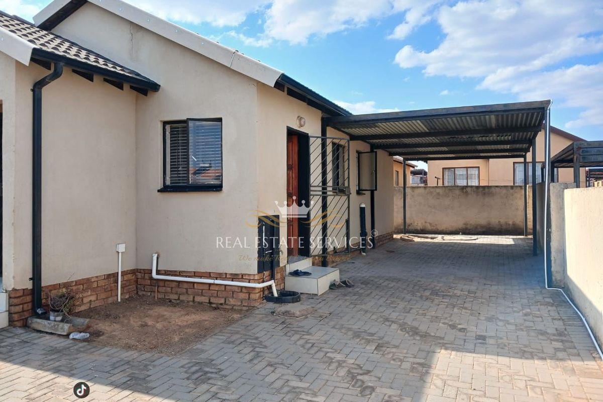 Front exterior view of the property featuring a paved driveway, a covered carport, and a secure entrance with a metal security gate.
