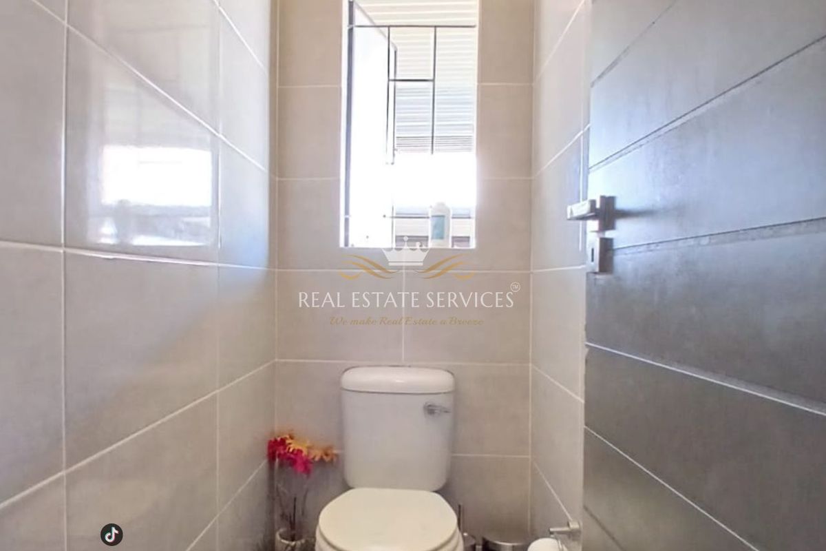 A compact guest bathroom featuring neutral ceramic wall tiles, a standard toilet, and a window with security bars.