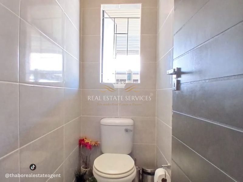 A compact guest bathroom featuring neutral ceramic wall tiles, a standard toilet, and a window with security bars.