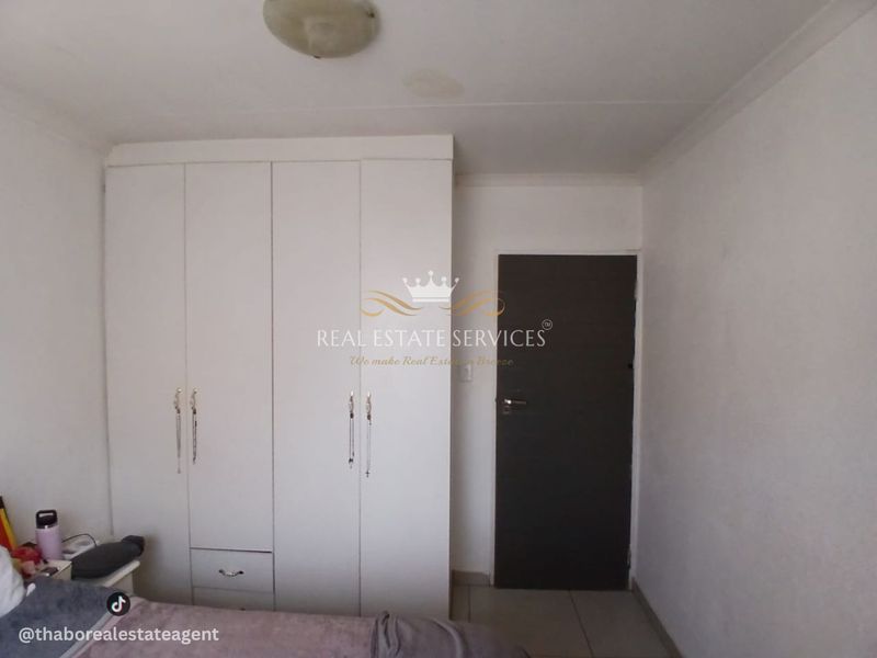 A bedroom featuring a built-in white wardrobe and a dark internal door, with visible ceiling staining requiring attention.