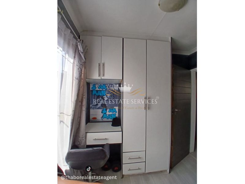 A bedroom featuring a white built-in wardrobe with an integrated desk unit and laminate flooring.