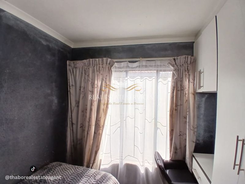 A bedroom featuring built-in cabinetry and a desk, with dark textured wall finishes and natural light through a window.