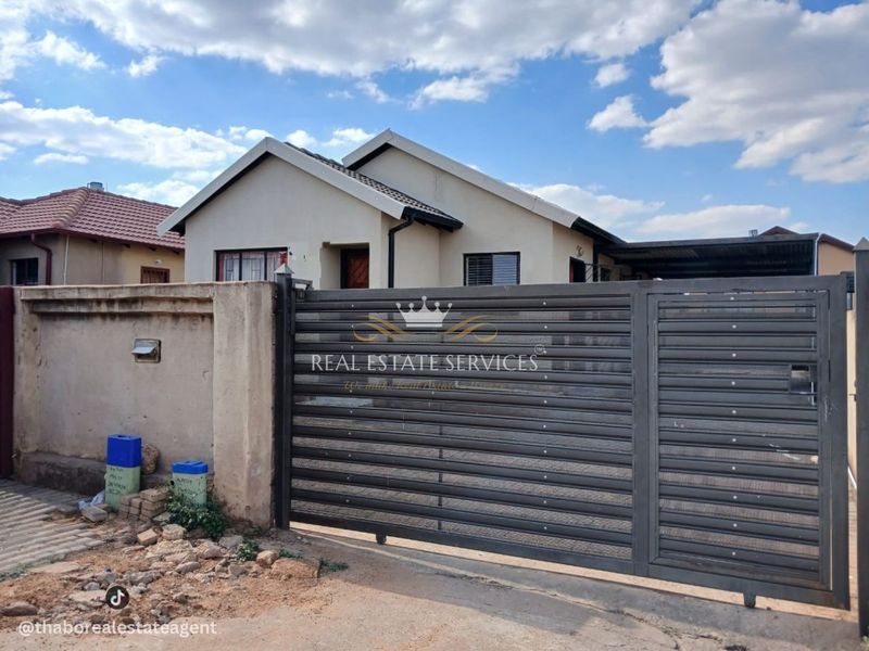 Front view of a residential house featuring a sliding metal gate, perimeter wall, and tiled roof structure.