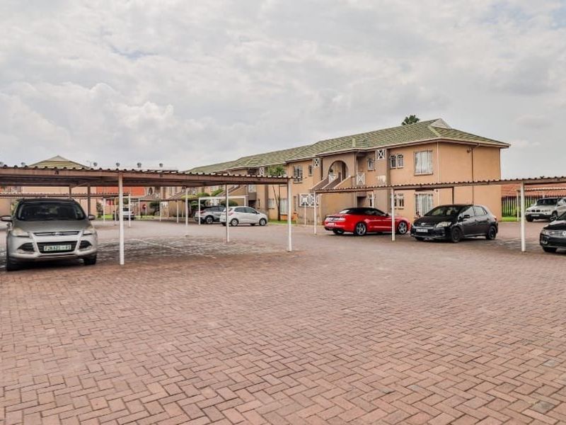 Exterior view of an apartment complex featuring a paved parking area with covered carports and multi-story residential units.