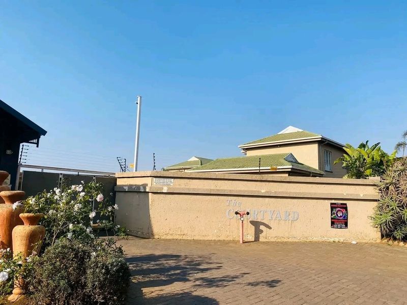 Front entrance view of The Courtyard apartment complex featuring a paved driveway, perimeter wall with electric fencing, and tiled roof structures.