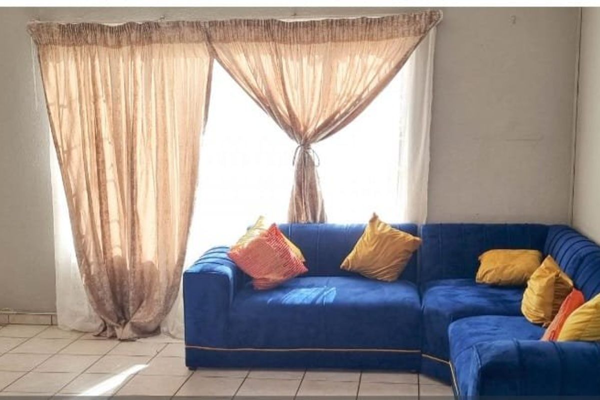 A living room area featuring tiled flooring and a large sliding door with curtains, providing access to the exterior.