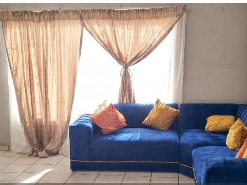 A living room area featuring tiled flooring and a large sliding door with curtains, providing access to the exterior.