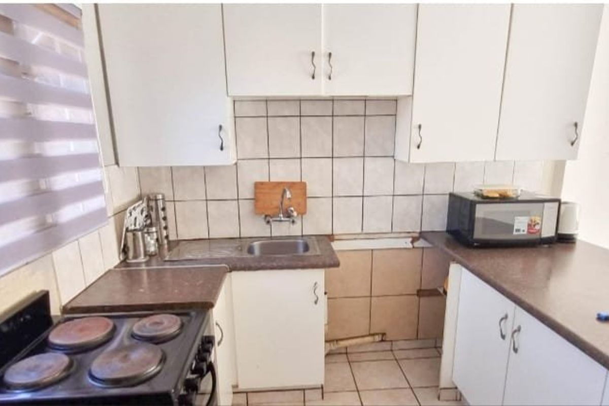 Compact kitchen featuring white cabinetry, laminate countertops, a stainless steel sink, and an electric stove, requiring some maintenance and cosmetic updates.