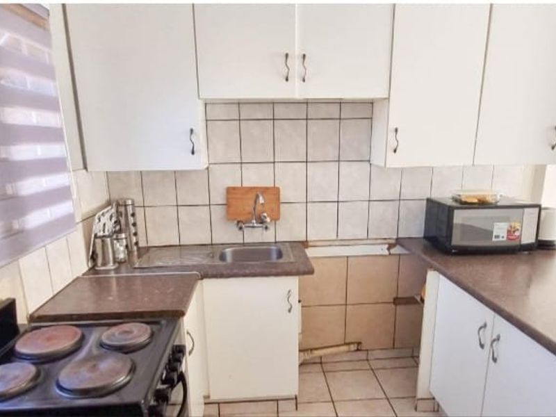 Compact kitchen featuring white cabinetry, laminate countertops, a stainless steel sink, and an electric stove, requiring some maintenance and cosmetic updates.