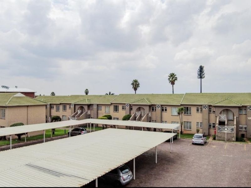 An elevated view of an apartment complex featuring multiple units with tiled roofs, a paved parking area, and covered carports.