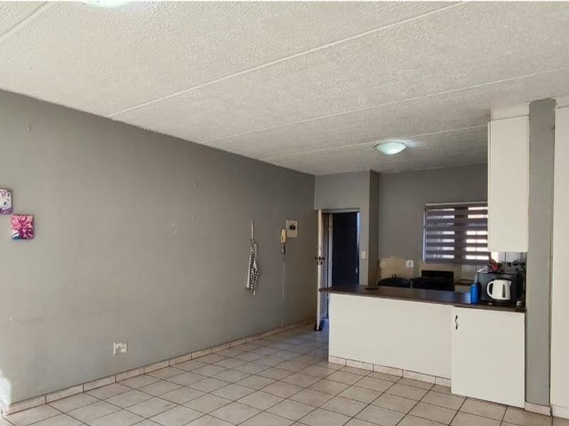 Open-plan living area featuring tiled flooring, a breakfast counter, and built-in storage cupboards, offering a functional layout ready for personalization.