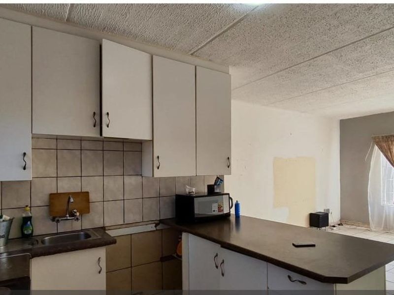 Open-plan kitchen and living area featuring built-in cabinetry, tiled backsplash, and tiled flooring, offering a functional layout in need of cosmetic updates.