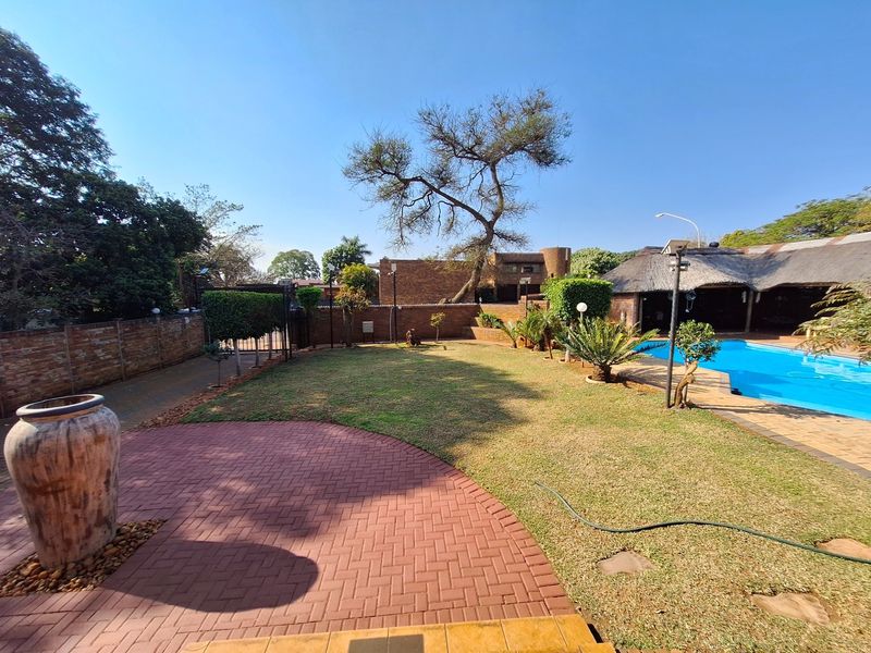 Spacious outdoor area featuring a swimming pool, manicured lawn, brick paved patio, and a thatched roof entertainment structure.