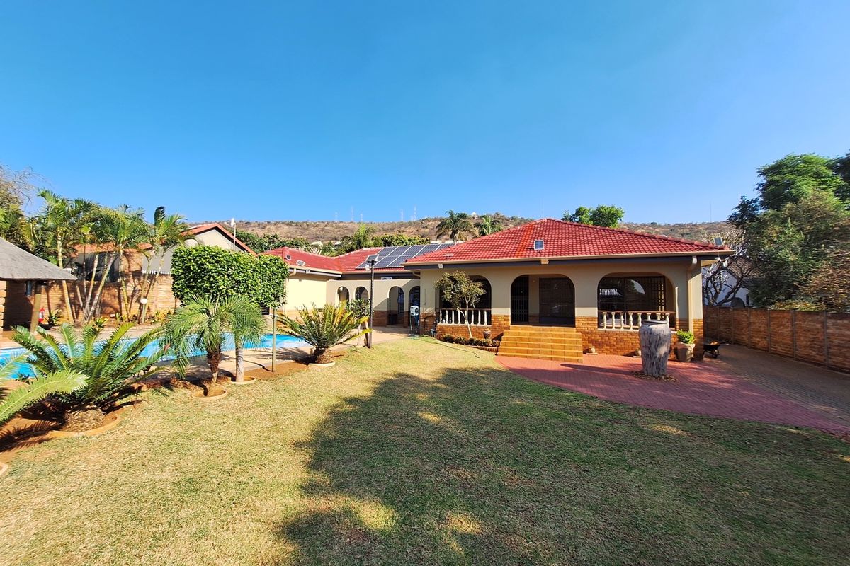 Rear view of the property featuring a landscaped garden, swimming pool, covered patio area, and solar panels installed on the tiled roof.