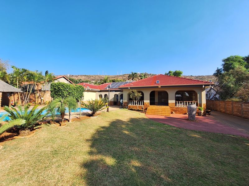 Rear view of the property featuring a landscaped garden, swimming pool, covered patio area, and solar panels installed on the tiled roof.
