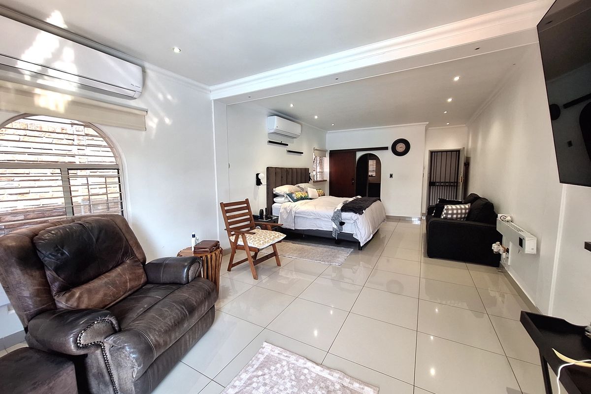 Spacious bedroom featuring tiled flooring, recessed downlighting, and split-system air conditioning, with an open-plan layout and arched architectural details.
