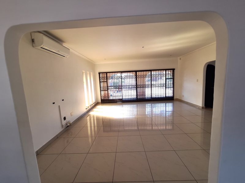 Spacious, empty living area featuring neutral tiled flooring, a wall-mounted air conditioning unit, and large sliding glass doors with security gates.