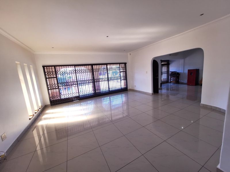 Spacious, light-filled living area featuring polished tile flooring, an arched entryway, and a secure sliding gate leading to the exterior.