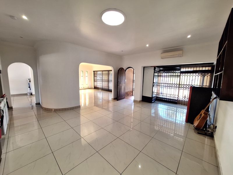 Spacious living area featuring polished tiled flooring, arched architectural details, recessed lighting, and wall-mounted air conditioning, offering a bright and open layout.