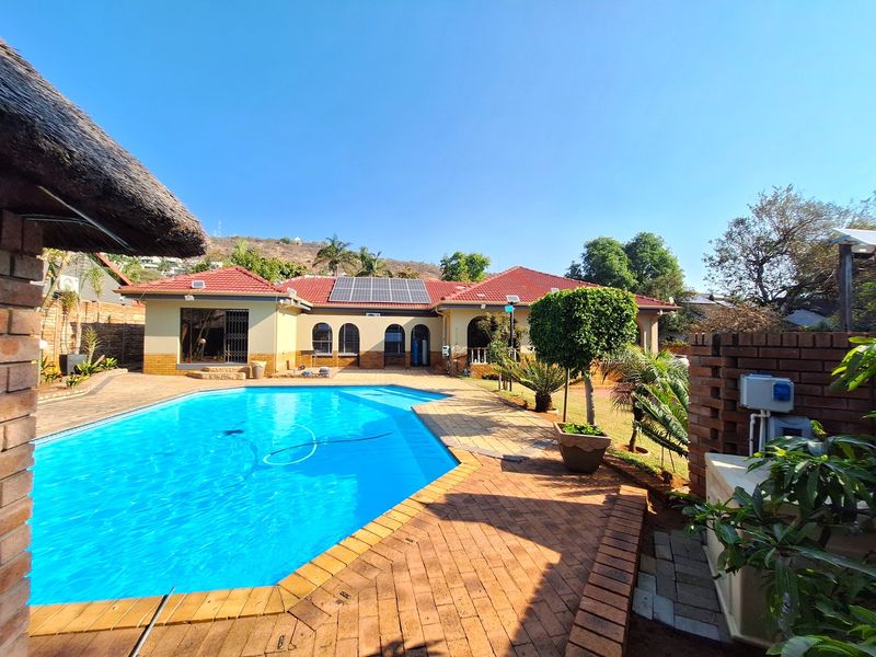 Spacious outdoor pool area featuring a large swimming pool, brick paving, and a house exterior equipped with solar panels and a tiled roof.