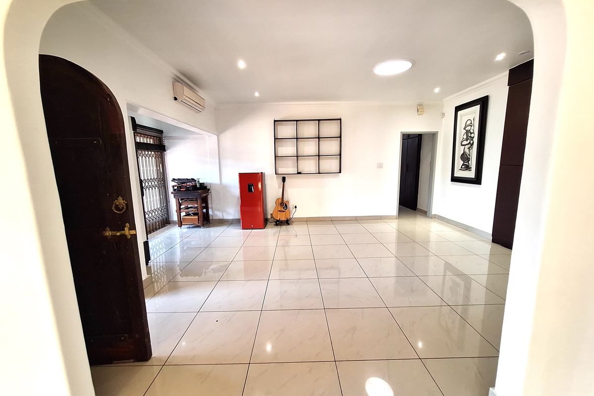 Spacious living area featuring neutral tiled flooring, recessed lighting, and a distinctive arched entryway, providing a clean and versatile space.