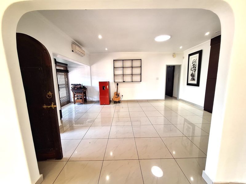 Spacious living area featuring neutral tiled flooring, recessed lighting, and a distinctive arched entryway, providing a clean and versatile space.